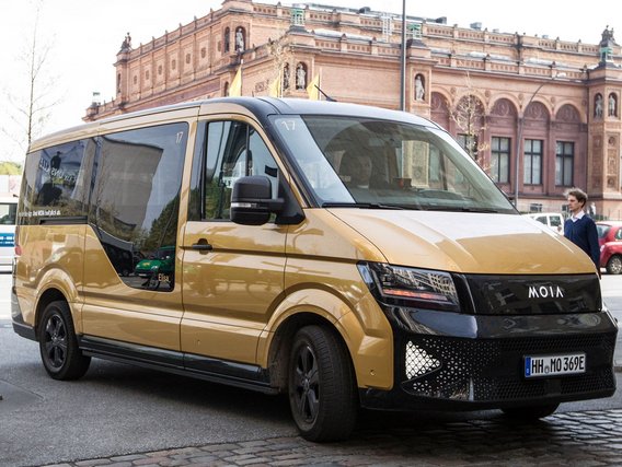 MOIA-Shuttle in goldener Lackierung vor einem historischen Backsteingebäude, vermutlich in Hamburg.
