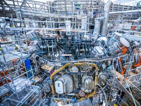 Eine extrem komplexe technische Anlage mit zahllosen Rohren, Leitungen und Metallstrukturen. Ein dichtes Geflecht aus Industrietechnik in Blau-, Silber- und Orangetönen.