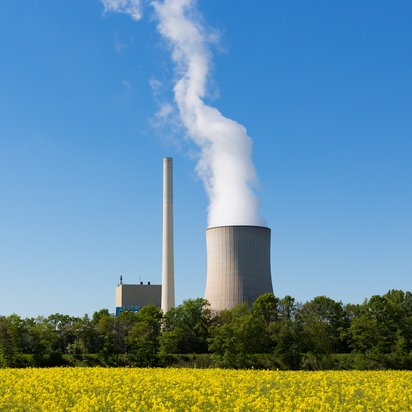 Dampfausstoß aus Kühlturm eines Kraftwerks bei blauem Himmel.
