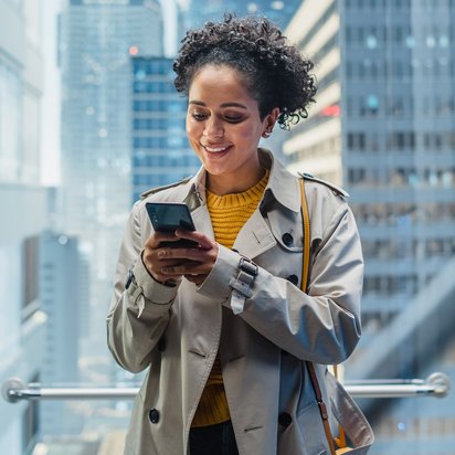 Eine Person steht vor hohen Bürogebäuden und bedient ein Smartphone.
