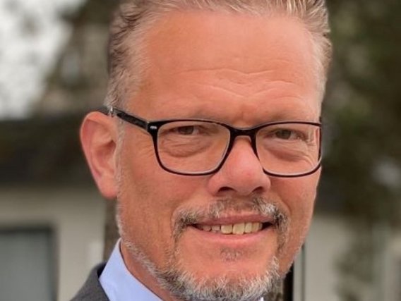 Holger Krumme im mittleren Alter mit grauem Haar, Brille und Bart lächelt in die Kamera. Er trägt ein formelles Hemd.