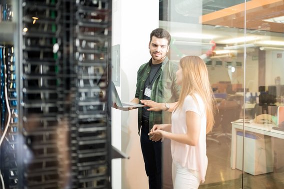 Zwei IT-Fachkräfte stehen im Serverraum und besprechen Daten auf einem Laptop vor einem Serverschrank