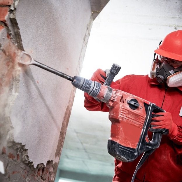 Worker in protective clothing demolishing a wall with a demolition machine
