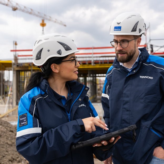 Zwei TÜV NORD-Mitarbeitende mit Helmen und Tablets im Gespräch auf einer Baustelle beim baubegleitenden Qualitätscontrolling