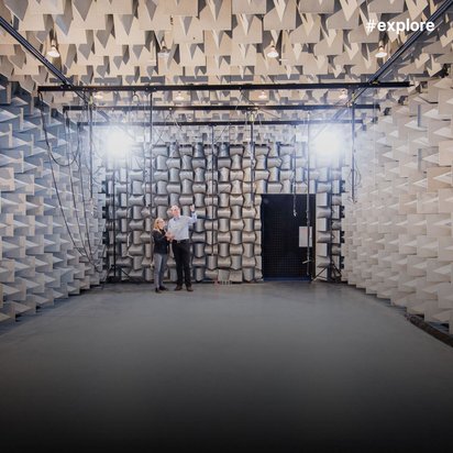 Große schalltote Kammer mit Akustikschaumstoff an allen Wänden; zwei Personen stehen in der Mitte unter Messausrüstung und Beleuchtung.