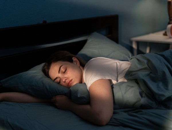 Frau schläft ruhig in einem Bett, umgeben von Kissen, in einem Schlafzimmer mit gedämpftem Licht