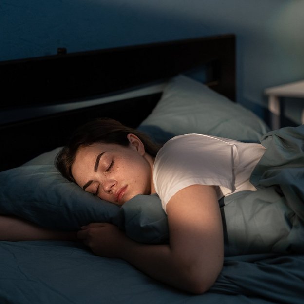 Frau schläft ruhig in einem Bett, umgeben von Kissen, in einem Schlafzimmer mit gedämpftem Licht