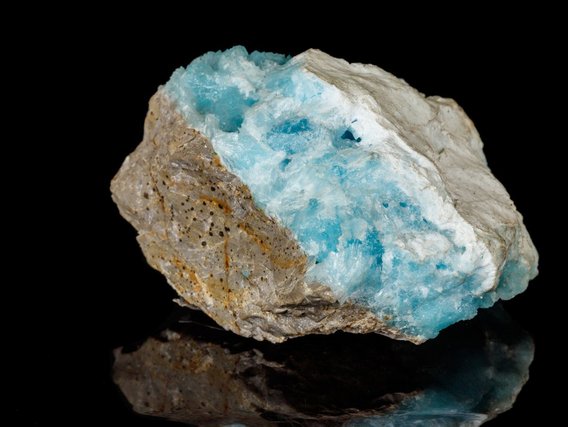 Mineralprobe mit leuchtend türkisblauen, kristallinen Bereichen neben beigefarbenen, porösen Gesteinspartien auf schwarzem Hintergrund.