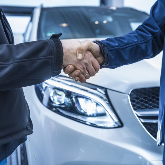 Handschlag zwischen einem Autohändler und Kunde vor einem Auto