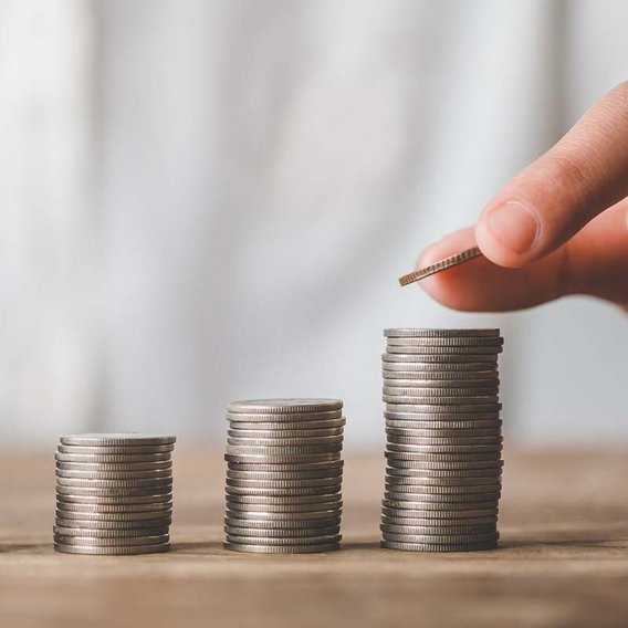 Eine Hand stapelt Münzen in aufsteigender Reihenfolge, symbolisiert finanzielle Förderung und Wachstum im Bereich Weiterbildung. Die Münzen sind auf einem Tisch angeordnet.