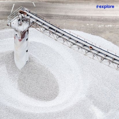 Eine industrielle Anlage mit Förderband auf einem großen Haufen weißen Granulats oder Kies in einer kargen Industrielandschaft.