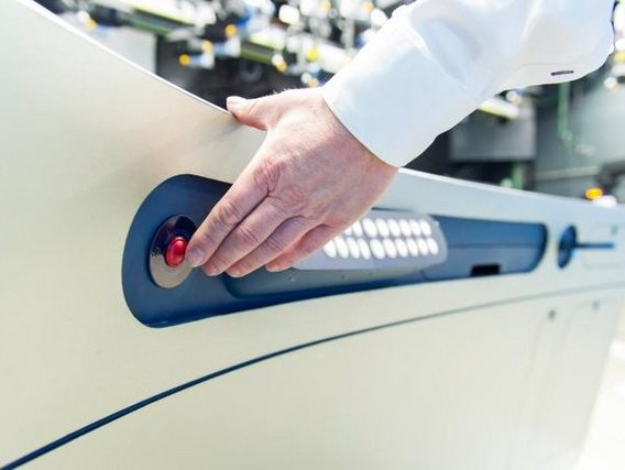 Eine Hand in weißem Laborkittel bedient einen roten Knopf auf einer Bedienleiste eines medizinischen oder wissenschaftlichen Gerätes.