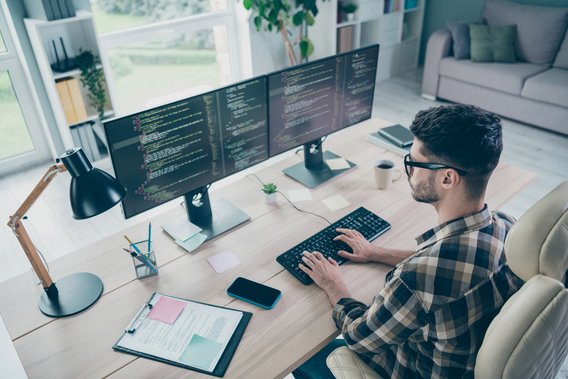 Programmierer sitzt vor zwei Monitoren mit Code und arbeitet konzentriert an einem Projekt im Homeoffice