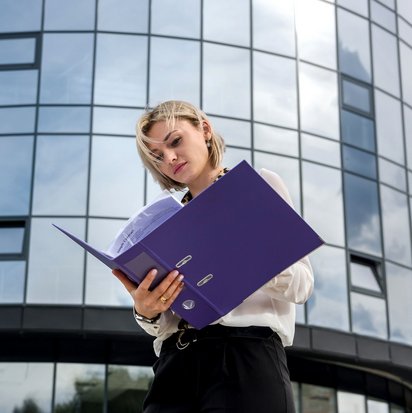 Junge Frau mit Aktenordner vor einem modernen Bürogebäude – Symbolbild zum Interview mit Referentin Miriam Bunke