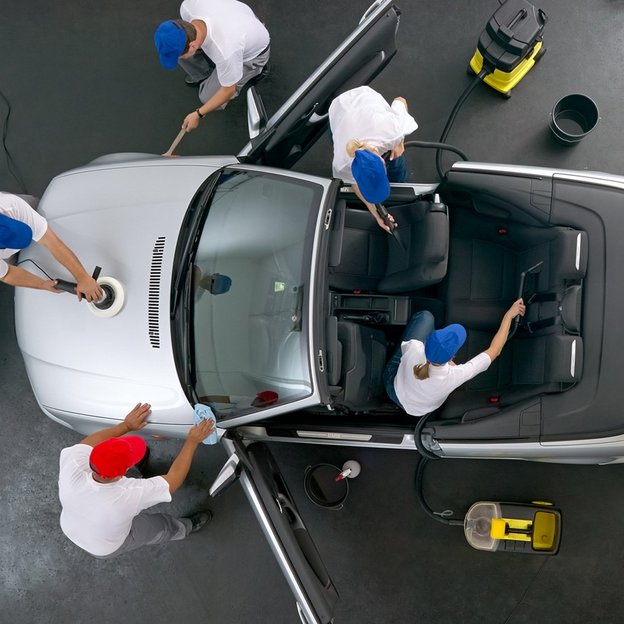 Mehrere Fachkräfte reinigen und polieren ein silbernes Cabriolet in einer Werkstatt, wobei sie sowohl das Äußere als auch das Innere des Fahrzeugs sorgfältig pflegen.