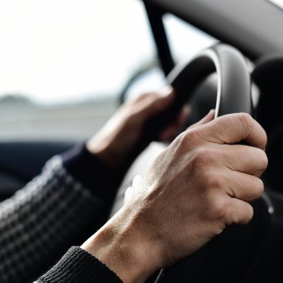 Mann mit beiden Händen am Lenkrad eines Autos.