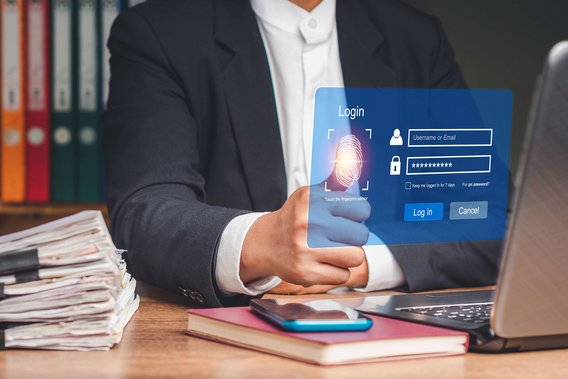 Person im Anzug nutzt Fingerabdrucksensor auf einem holografischen Login-Interface vor einem Laptop.