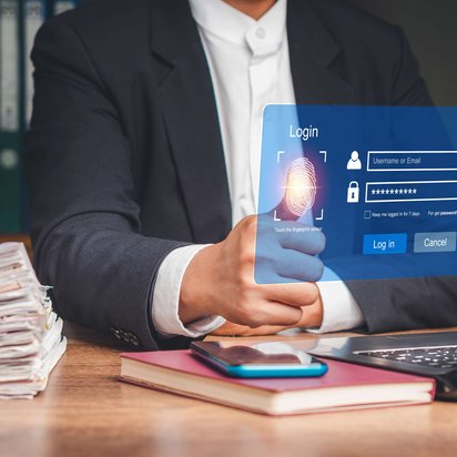 Person im Anzug nutzt Fingerabdrucksensor auf einem holografischen Login-Interface vor einem Laptop.