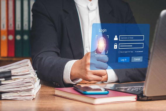 Person im Anzug nutzt Fingerabdrucksensor auf einem holografischen Login-Interface vor einem Laptop.