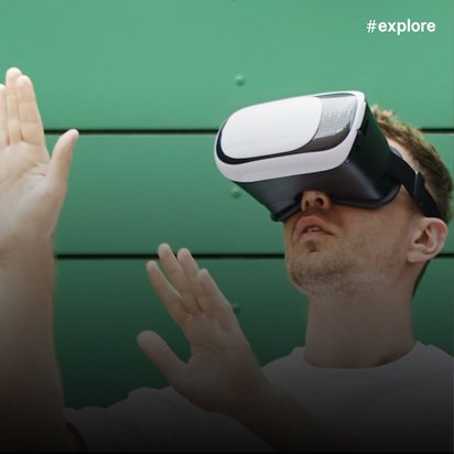 Eine Person trägt eine weiße VR-Brille und bewegt die Hände in einer gestikulierenden Bewegung vor einem grünen Wandhintergrund.