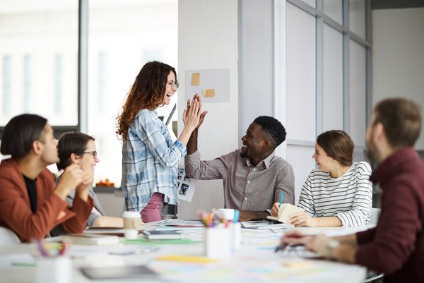 Team feiert gemeinsamen Erfolg mit High Five in kreativem Arbeitsumfeld