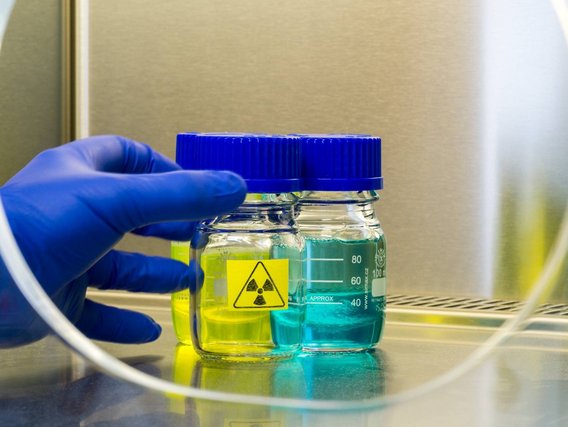 Laborprobe in Glasgefäßen mit Gefahrstoffsymbol, gehalten von einer Hand mit Schutzhandschuh.