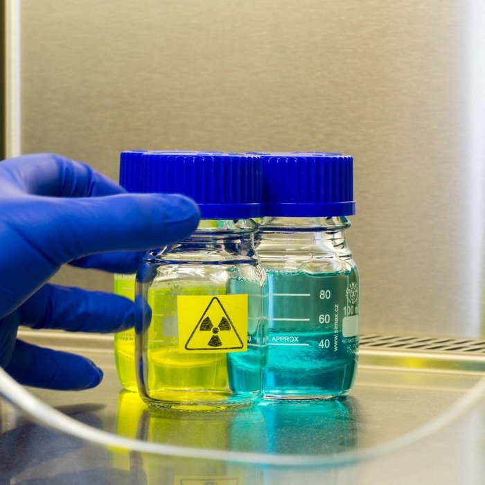 Laborprobe in Glasgefäßen mit Gefahrstoffsymbol, gehalten von einer Hand mit Schutzhandschuh.