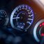 Nahaufnahme eines Fahrzeugcockpits mit beleuchtetem Tacho und Drehzahlmesser.