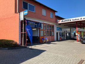 Offene Werkstatthalle mit Banner zur Neueröffnung der TÜV NORD Station Schöneck und zwei blauen Liegestühlen vor dem Eingang.