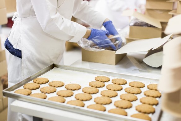 Arbeiterin verpackt Kekse in eine Schachtel. Sie trägt blaue Handschuhe.