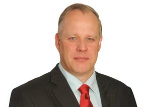 Volker Schultheiß im schwarzen Anzug mit roter Krawatte in einem professionellen Porträtfoto vor weißem Hintergrund.