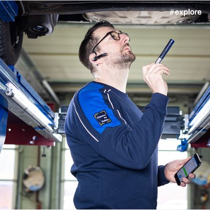Automechaniker unter einem Fahrzeug mit Smartphone und Diagnosegerät.