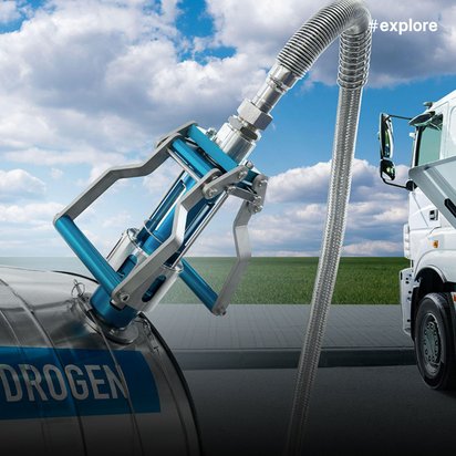 Wasserstofftankvorgang bei einem LKW mit metallischem Tankschlauch, der von einem blau markierten Wasserstofftank zu einem weißen Lastwagen führt. Der Tankvorgang findet vor blauem Himmel statt.