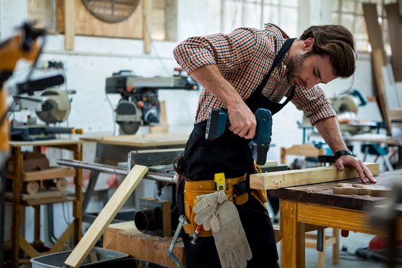 Handwerker bohrt konzentriert in ein Holzstück in einer Werkstatt.