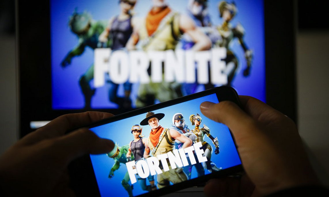 Ein Smartphone zeigt das Fortnite-Logo mit mehreren Spielcharakteren, während im Hintergrund ein größerer Bildschirm dasselbe Spielbild mit den bunten Avataren auf blauem Hintergrund wiedergibt.
