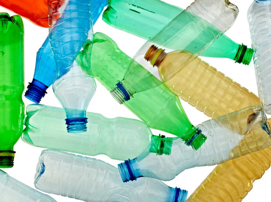 Verschiedene leere Plastikflaschen in bunten Farben (grün, blau, gelb, transparent) liegen chaotisch übereinander auf weißem Hintergrund.