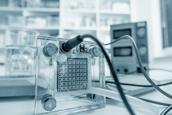 Im Vordergrund eine Brennstoffzelle auf einem Tisch in einem Labor