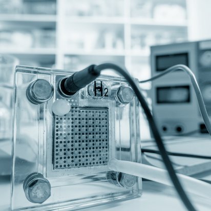 Im Vordergrund eine Brennstoffzelle auf einem Tisch in einem Labor