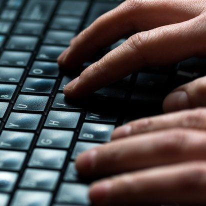 Großaufnahme zweier Hände, die auf einer schwarzen PC-Tastatur tippen.