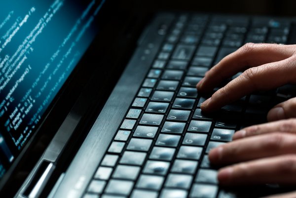 Nahaufnahme von Händen, die auf einer Tastatur tippen, mit Code auf einem Laptopbildschirm.