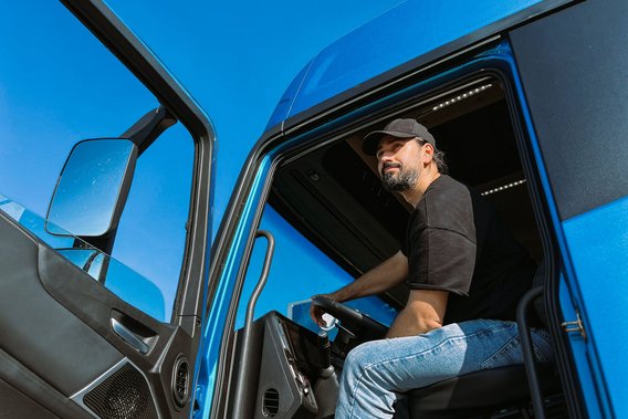 Lkw-Fahrer mit Basecap sitzt in einem blauen Lkw und blickt aus der geöffneten Tür
