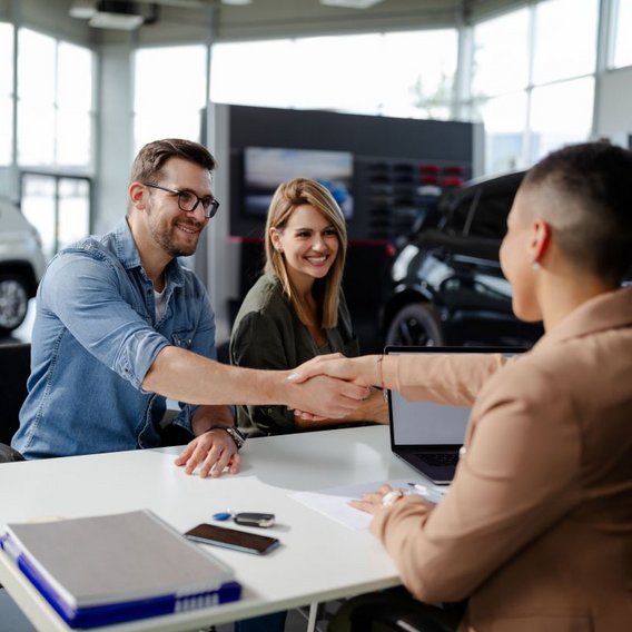 Im Autohaus sitzen ein Mann und eine Frau am Schreibtisch und schließen Vertrag ab