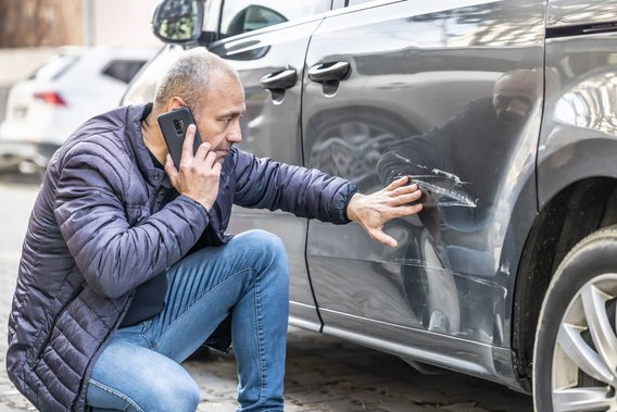 Mann inspiziert Kratzer an der Autotür und telefoniert