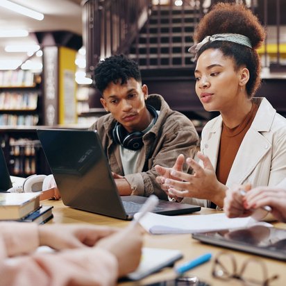 Gruppe junger Menschen arbeitet gemeinsam mit Laptops und Notizen in einer Bibliothek