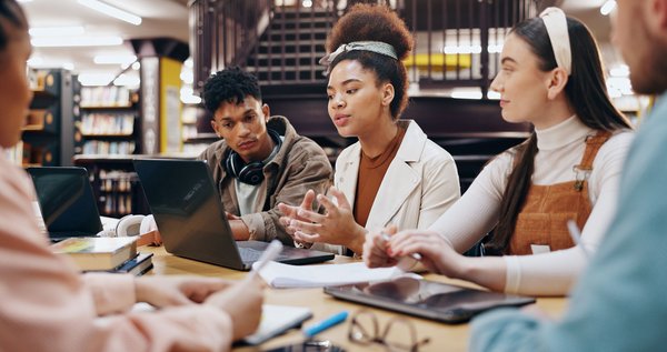 Gruppe junger Menschen arbeitet gemeinsam mit Laptops und Notizen in einer Bibliothek