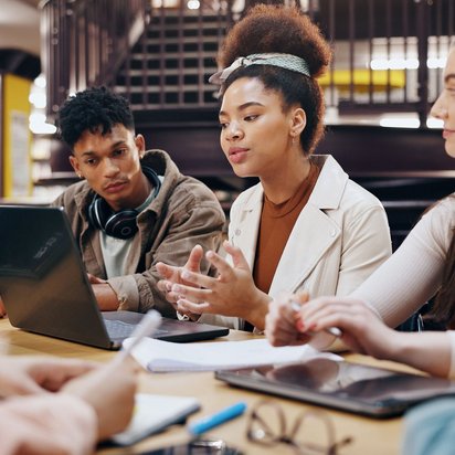 Gruppe junger Menschen arbeitet gemeinsam mit Laptops und Notizen in einer Bibliothek