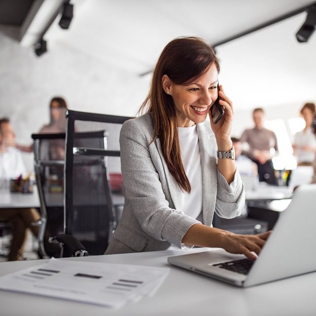 Mitarbeiterin am Telefon, die an einem Laptop arbeitet und in einem modernen Büroumfeld sitzt