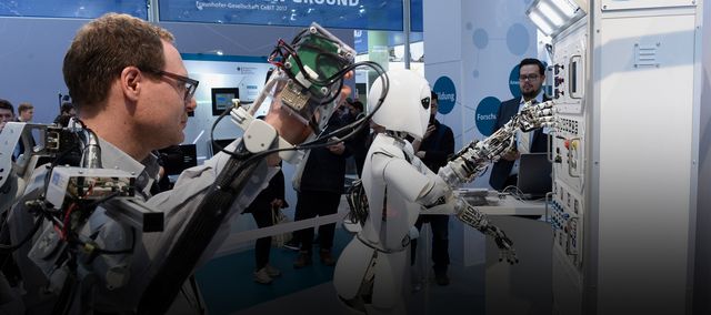 Ein Mann und ein Roboter arbeiten auf der CEBIT Hand in Hand