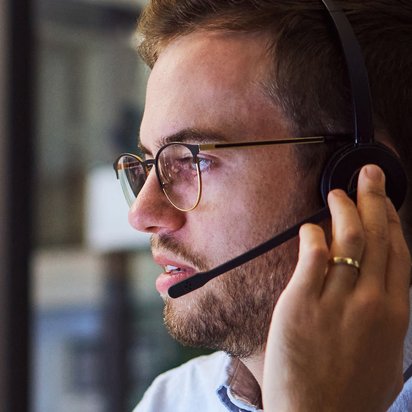 Ein Mann blickt zur Seite während er an das Headset fass, mit dem er gerade telefoniert.