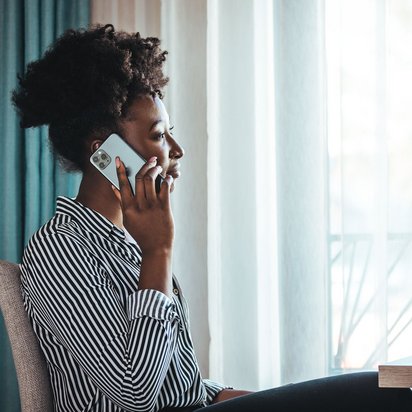 Frau mit lockigem Haar telefoniert mit dem Smartphone und blickt nachdenklich aus dem Fenster